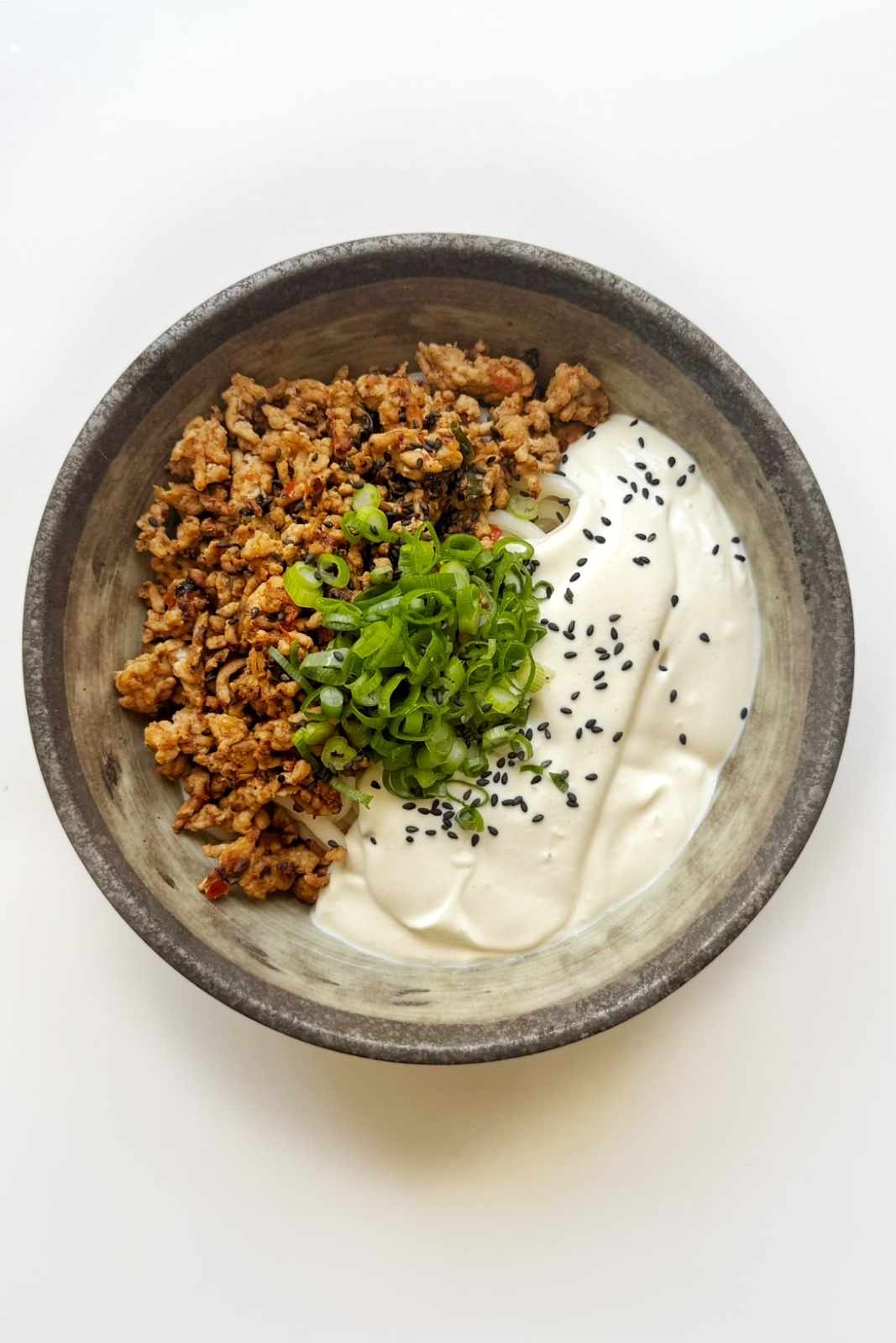 Stone bowl of creamy mapo tofu udon with blended silken tofu sauce, spicy ground pork, scallions and sesame seeds, the viral silken tofu noodle dish.