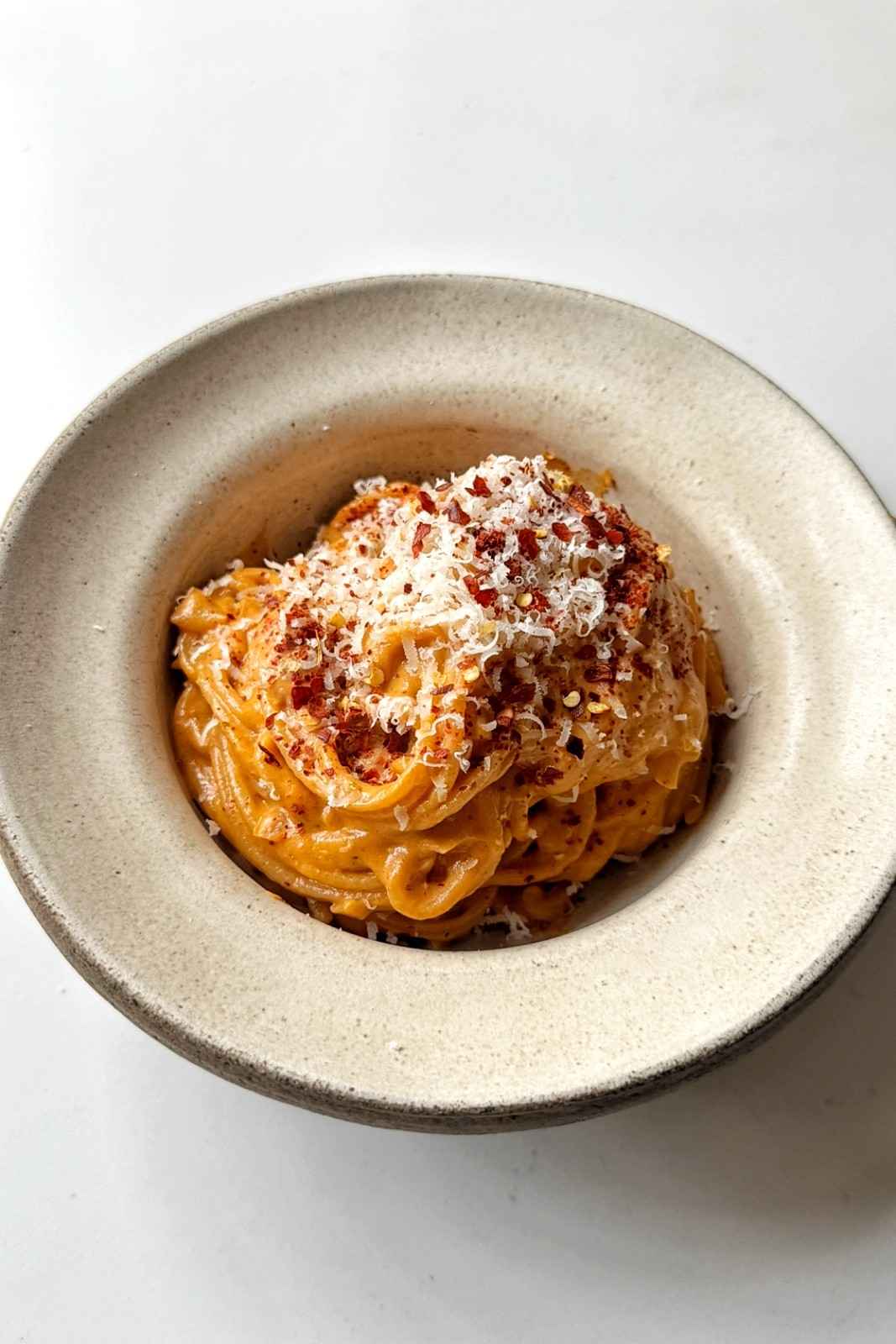 Creamy sun-dried tomato spaghetti in a speckled bowl, topped with grated Parmesan and chili flakes.