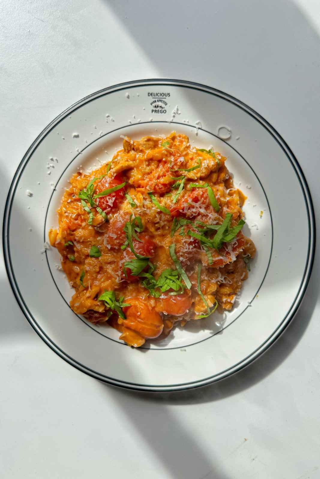 Creamy tomato orzo with cherry tomatoes, topped with grated Parmesan and fresh basil, in a white rimmed bowl.