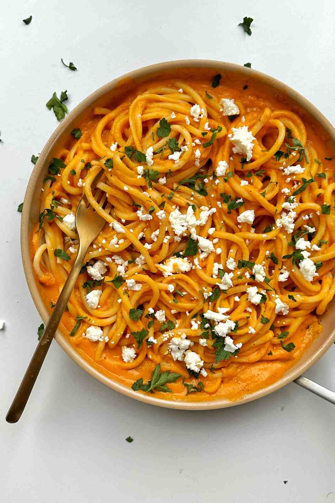 Creamy sweet potato pasta sauce coating spaghetti, topped with crumbled feta and parsley, in a cream bowl.