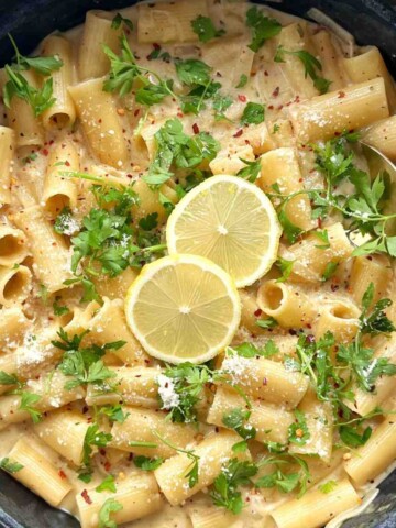 Creamy lemon Boursin pasta with rigatoni in a black pan, topped with parsley, chili flakes, Parmesan and lemon slices.
