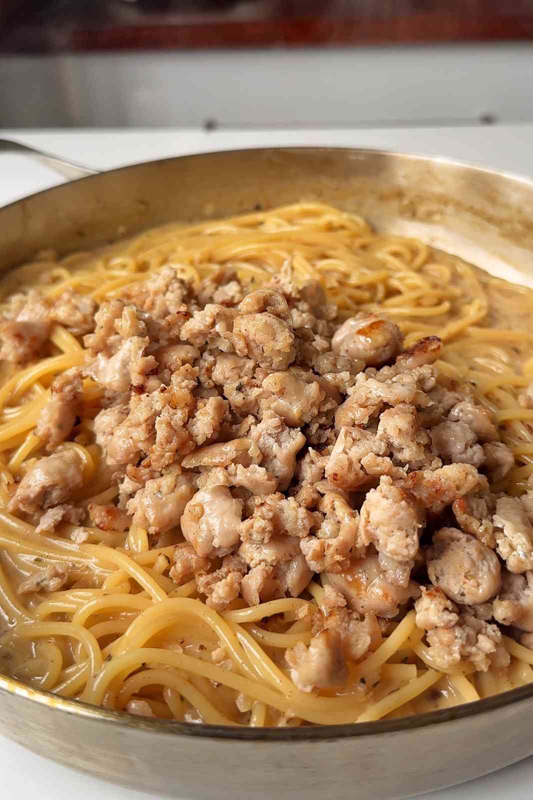 Adding sausage meat back into the spaghetti cream pan.