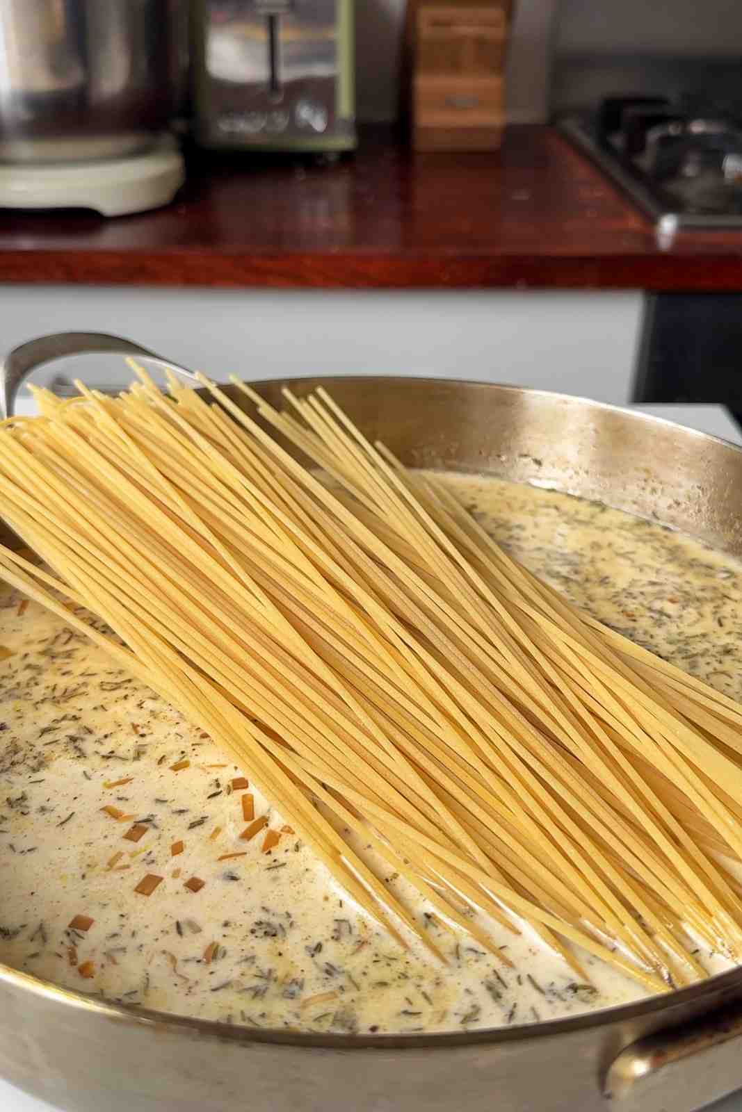 Adding spaghetti into the pan to cook the sausage pasta.
