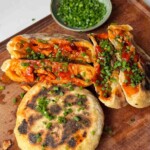 Fire chicken stuffed flatbreads with chopped chives on a wooden chopping board.