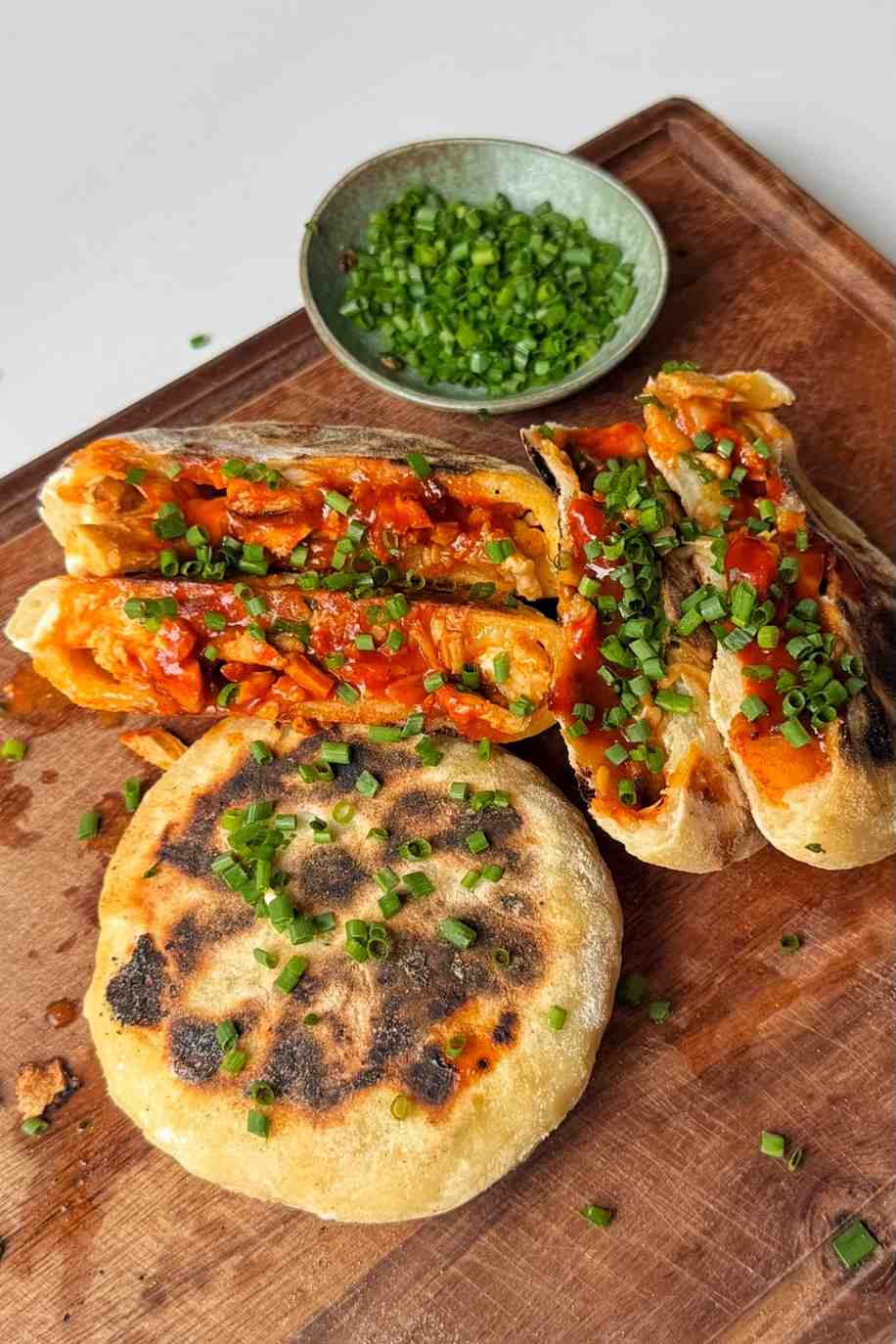 Fire chicken stuffed flatbreads with chopped chives on a wooden chopping board.