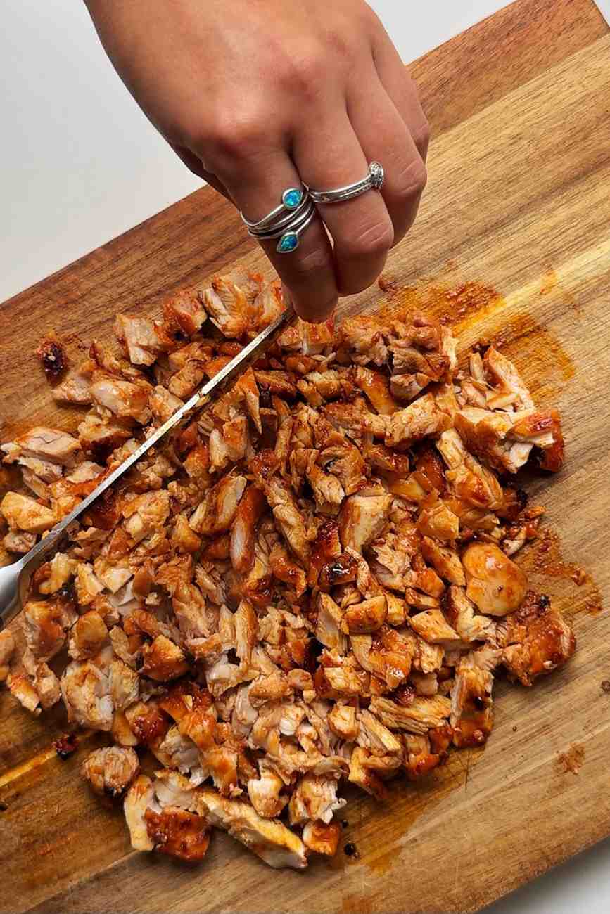 Chopping up chicken thighs on a wooden chopping board.