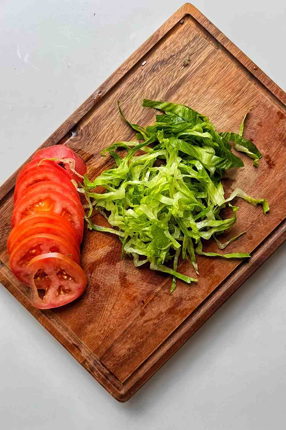 Sliced lettuce and tomato on a wooden chopping board.