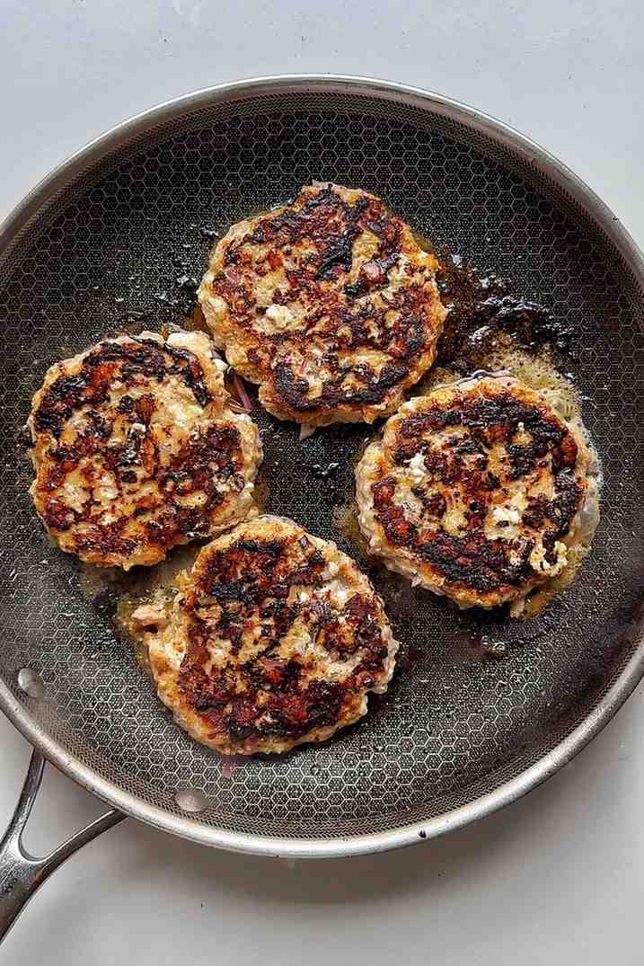 Greek burger patties frying in a pan.