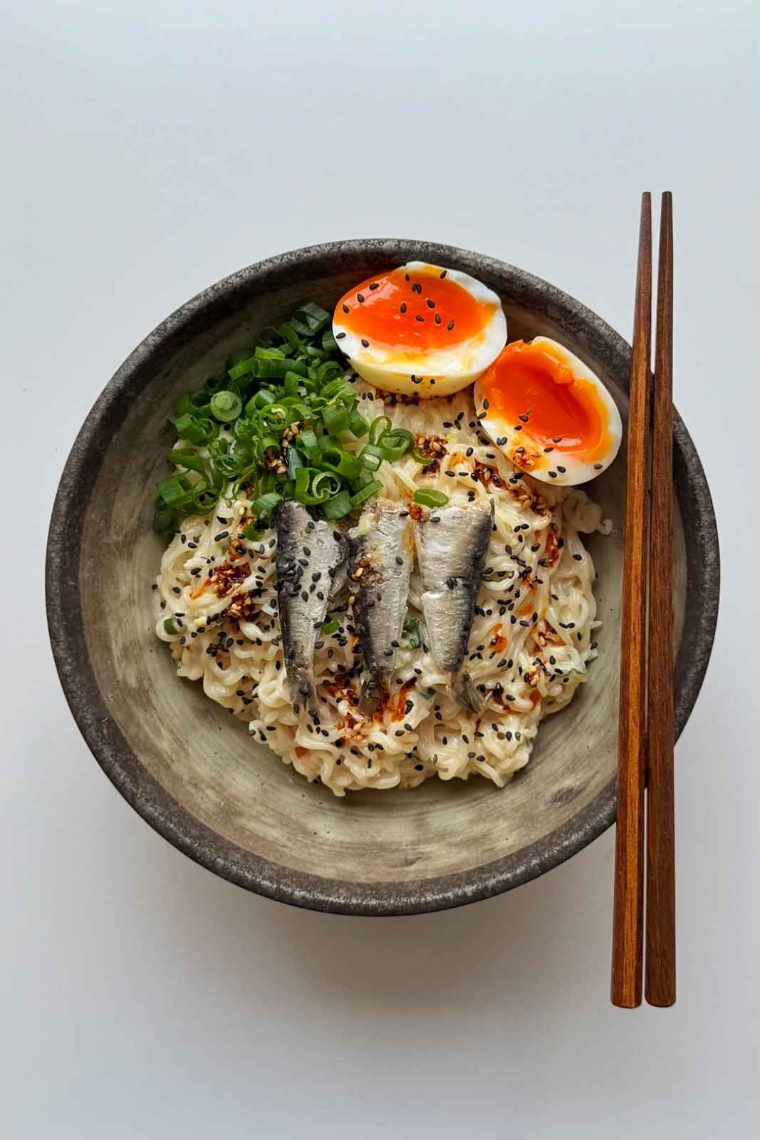 sardine ramen with jammy egg, scallions, and chopsticks.
